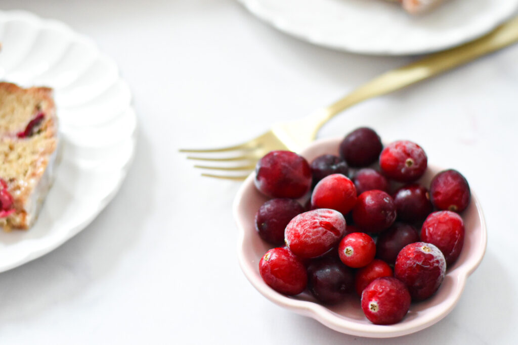 cranberries in a bowl next to a plate with cranberry bread on it