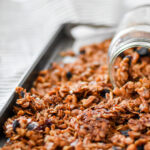 crunchy gingerbread granola on a baking tray, pouring out of a mason jar