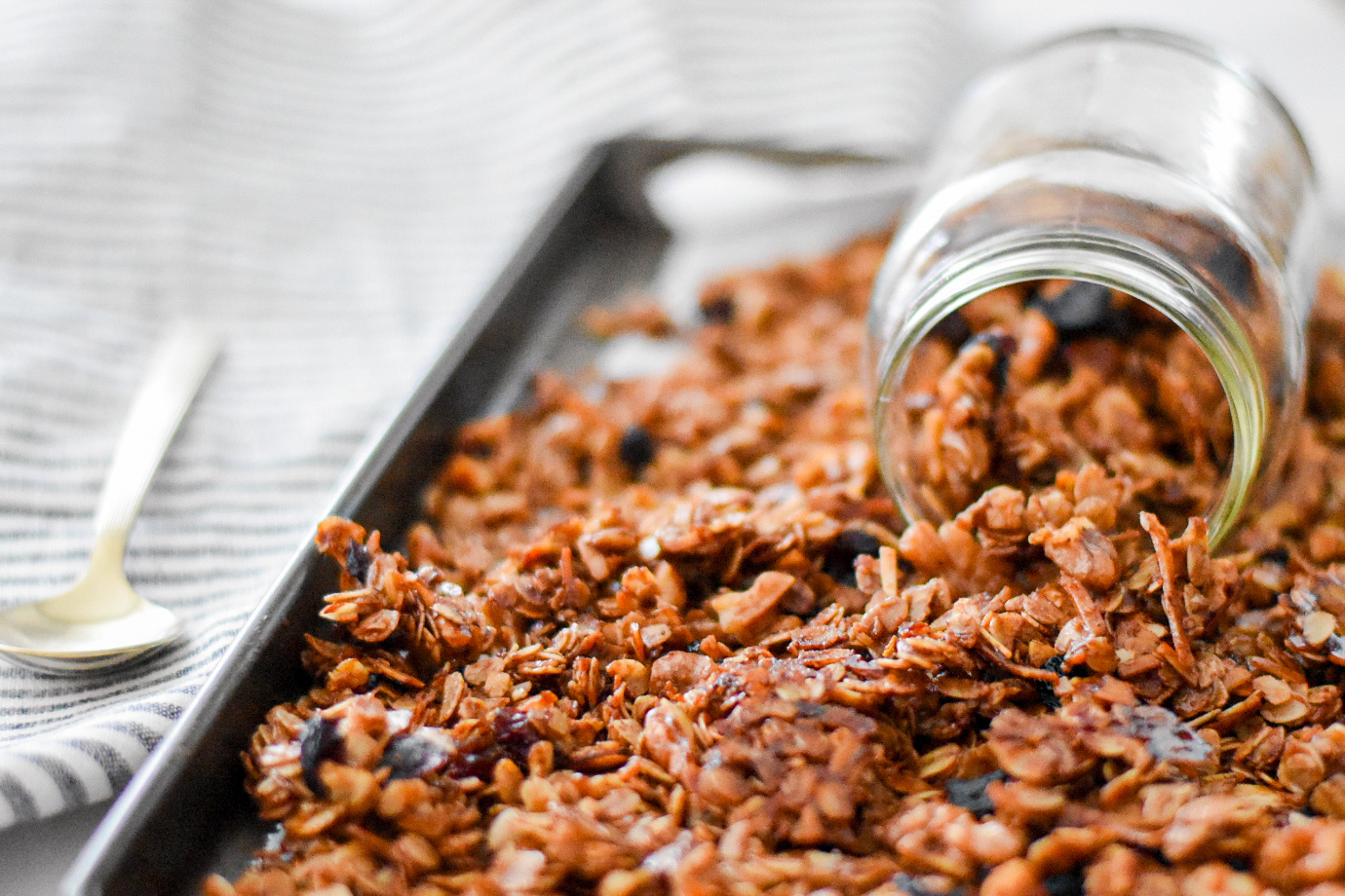 crunchy gingerbread granola on a baking tray, pouring out of a mason jar