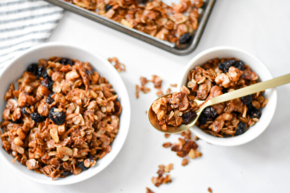 bowl of gingerbread granola on a table next to a smaller bowl with gingerbread granola, and a tray of gingerbread granola