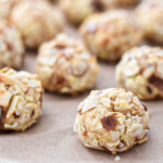 Close-up of a rum-buttered almond cookie with a golden, toasty almond coating, showcasing its pillowy, tender texture. A stack of almond cookies